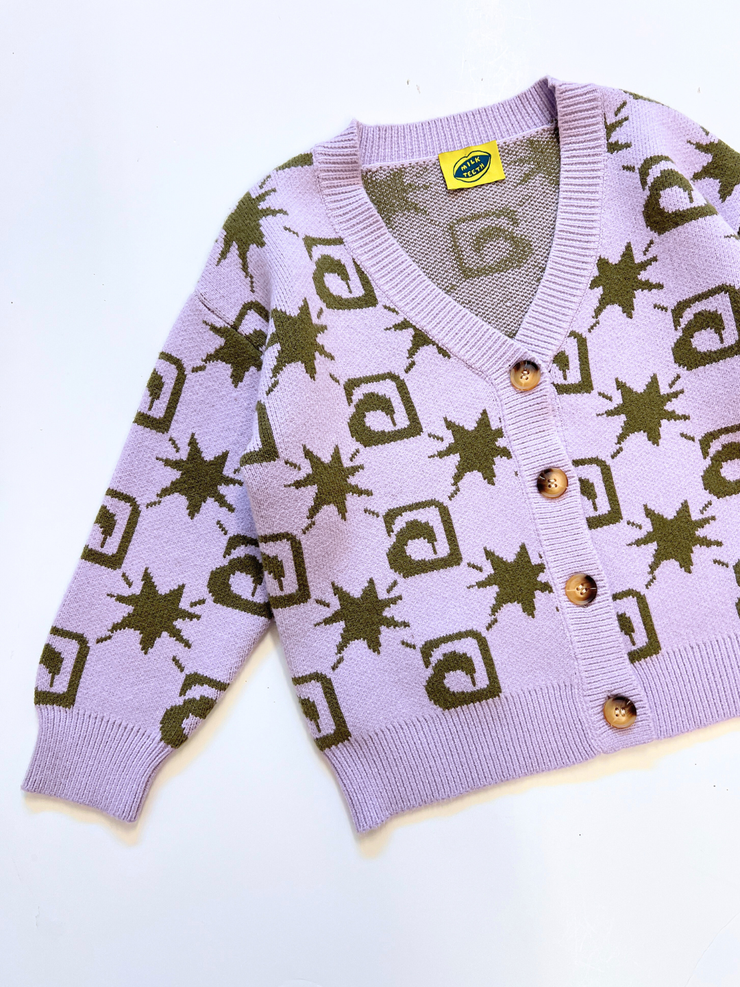 Lavender | The TRELLIS CARDIGAN is a lavender sweater featuring olive green geometric and star patterns, wooden buttons, and a yellow collar tag, displayed flat on a white background.
