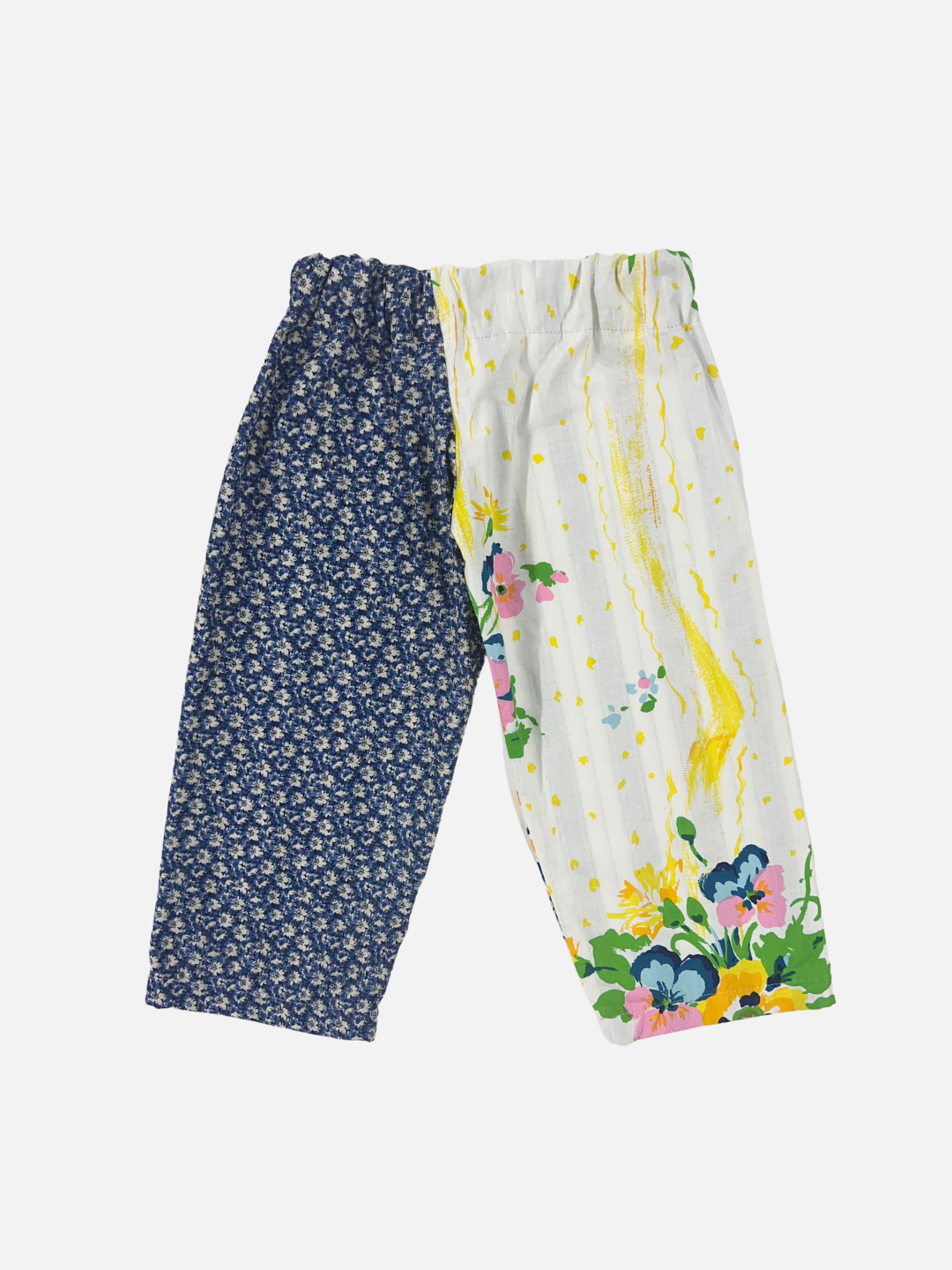 Front view of kid's patchwork pant. Left leg - white flower on navy. Right Leg - yellow splashes and flowers.