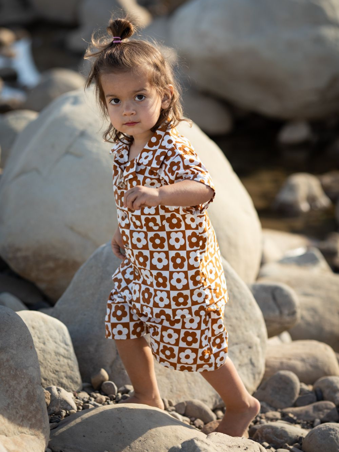 Terracotta | Child climbing over rocks wearing a kids' shirt and shorts set in a checkerboard pattern of terracotta brown and white flowers