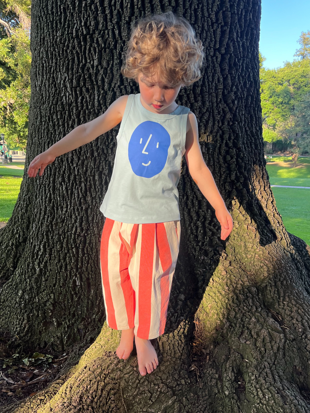 A child is wearing the Potato Face tank top with red striped pants