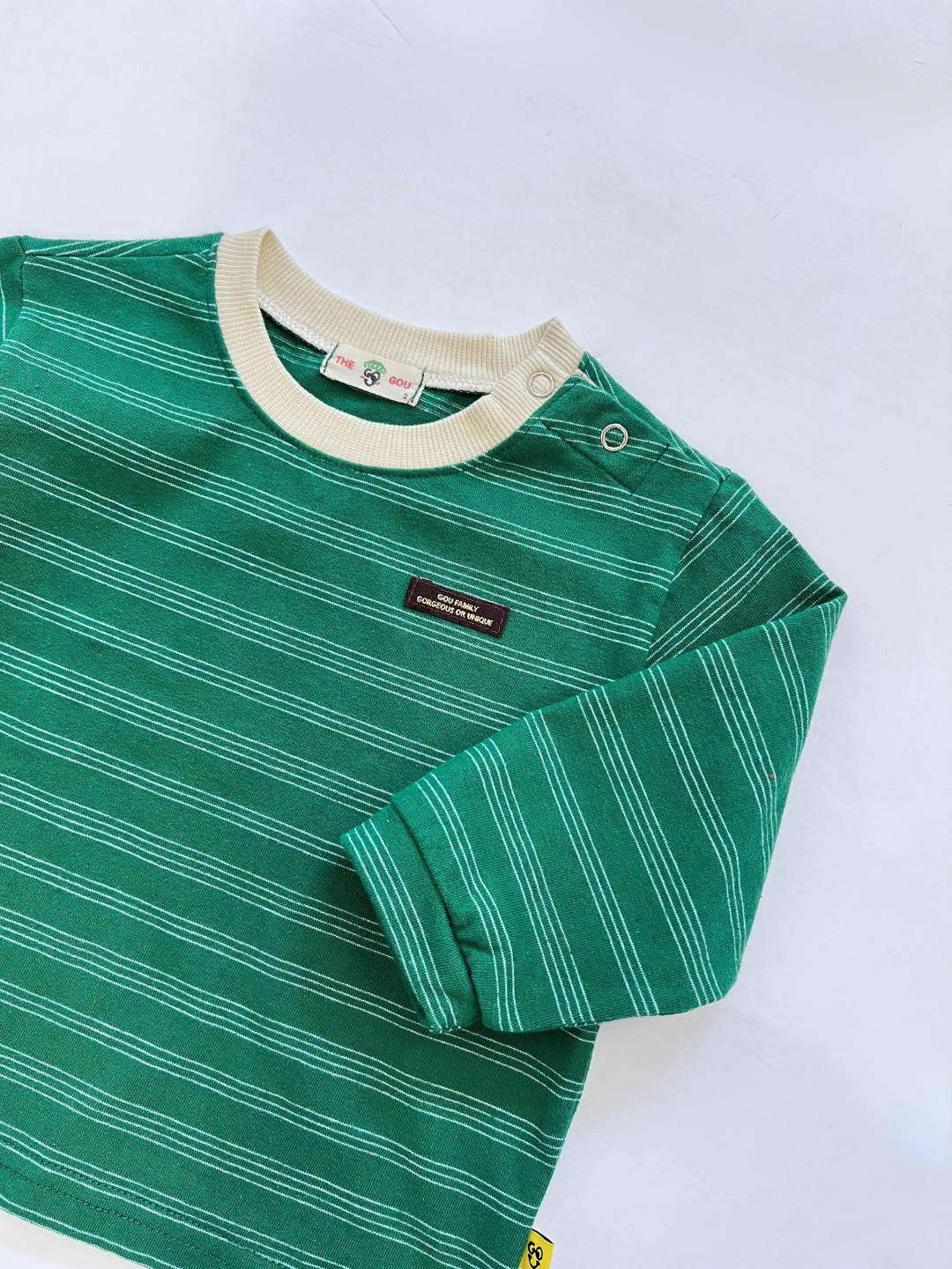 The MINI STRIPE LONGSLEEVE is a green and white baby tee with a beige collar and snap buttons on the shoulder, inspired by Korean baby clothing—made from cozy cotton and displayed flat on a white background.