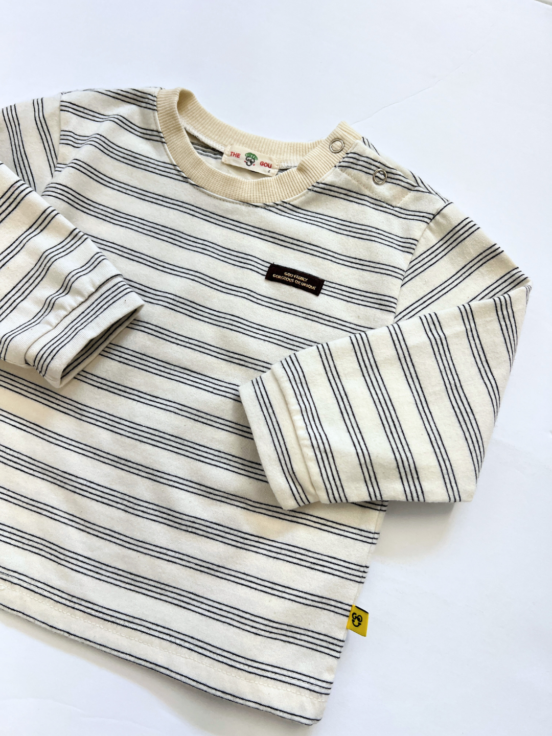 The MINI STRIPE LONGSLEEVE is a Korean-style cotton baby tee with black stripes on cream, featuring a small front label and shoulder button detail.