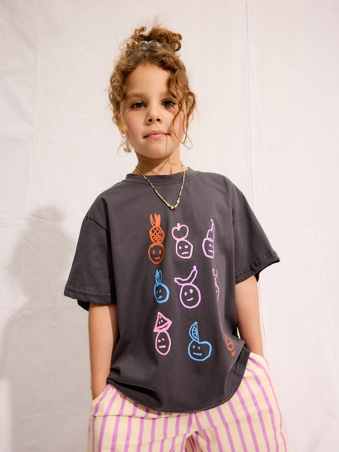 A child is wearing a Charcoal Fruit face tee with Pine Pants