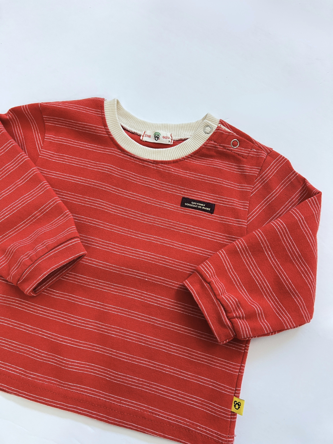 Red | The MINI STRIPE LONGSLEEVE is a stylish red baby top with thin white stripes, a cream collar, two snap shoulder buttons, and a small black chest label—perfect for fans of trendy Korean baby clothing.
