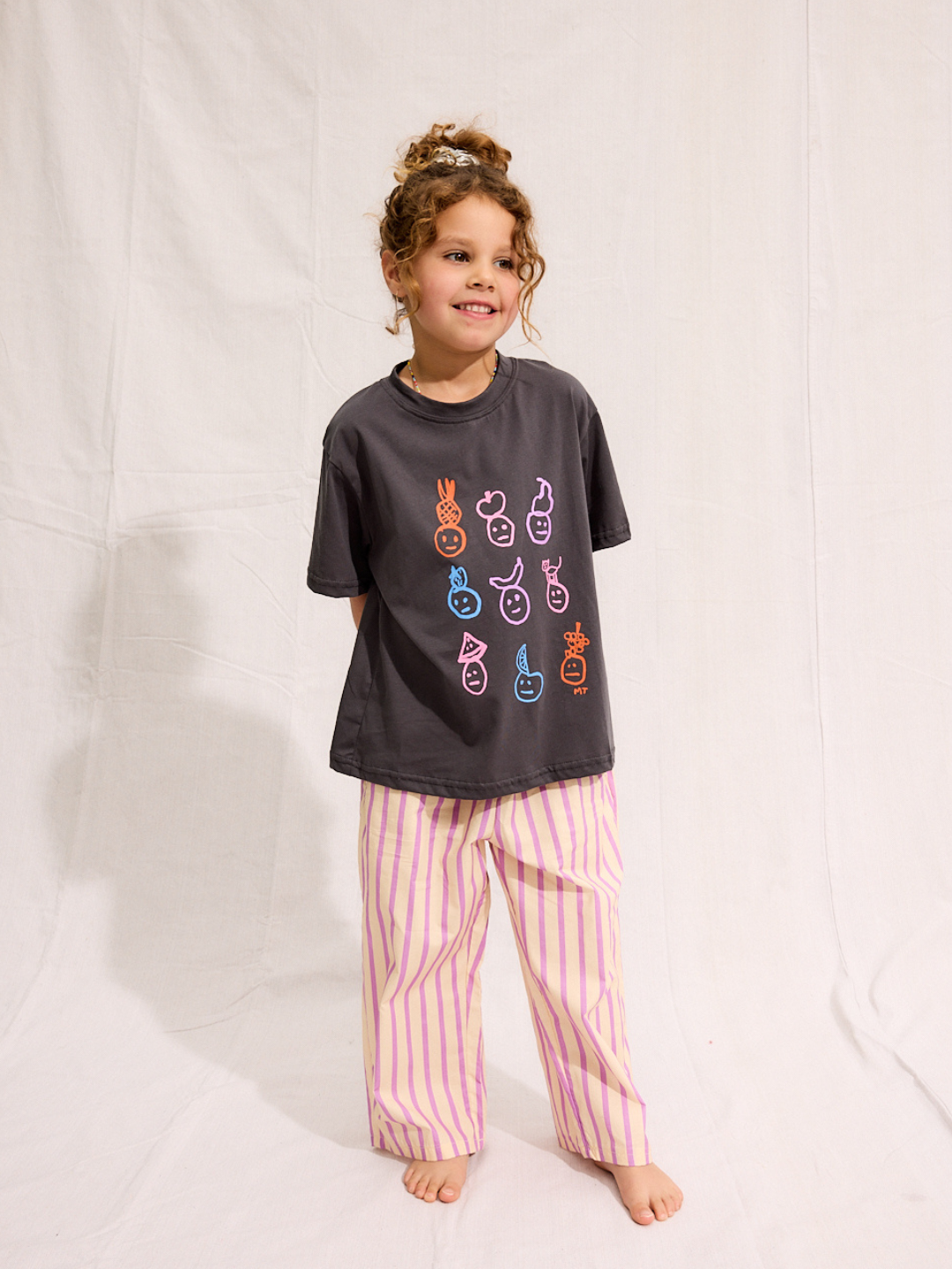 A child is wearing a Charcoal Fruit face tee with Pine Pants
