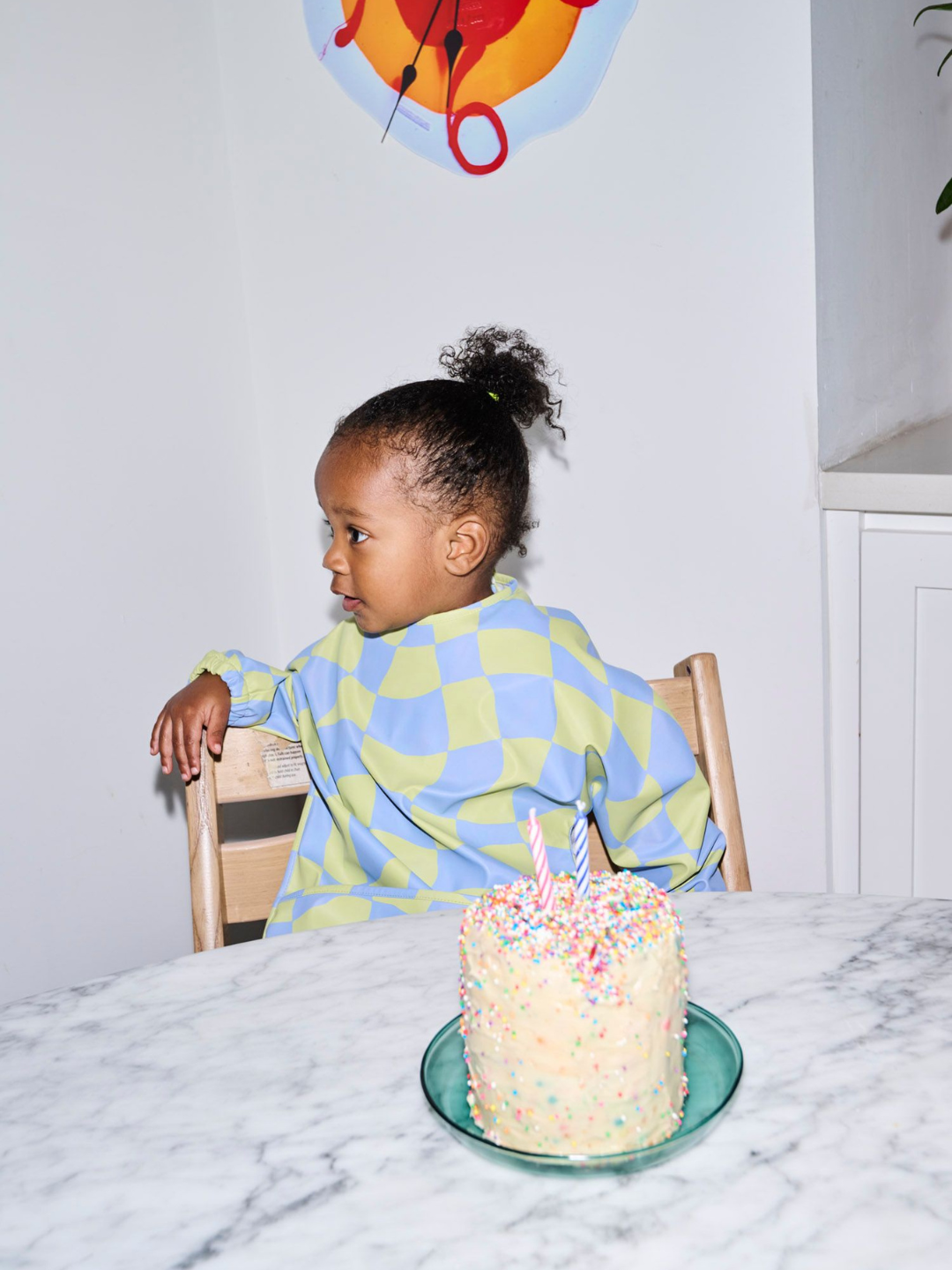 Green Checkers | A child wearing the long sleeve light green and blue wavy checked bib with a front pocket.