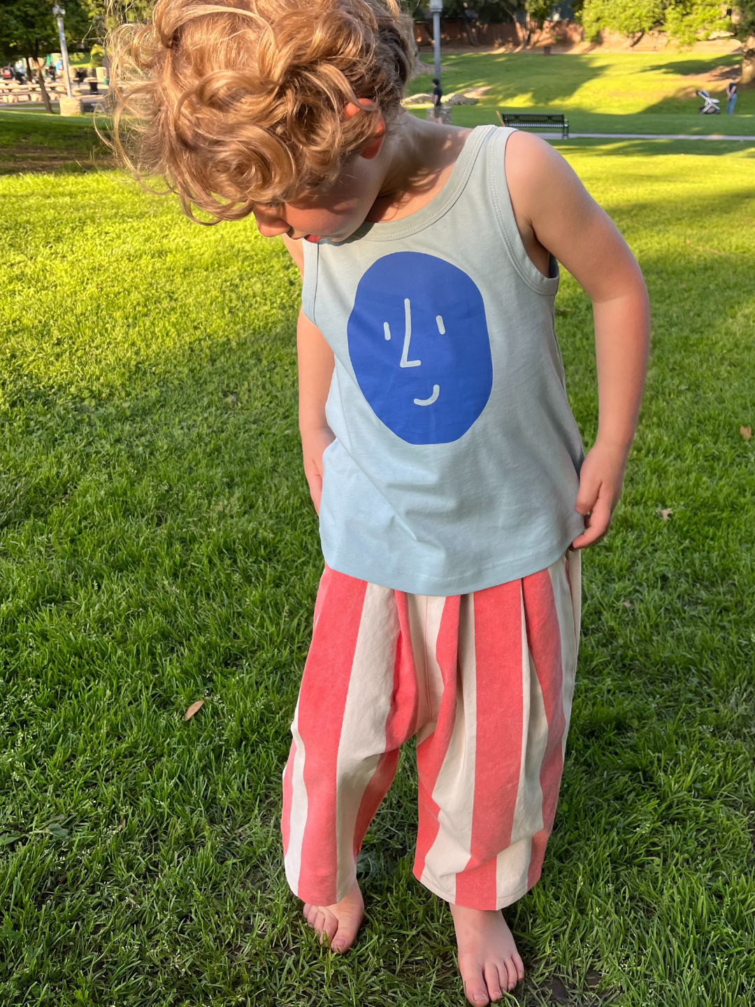 A child is wearing the Potato Face tank top with red striped pants