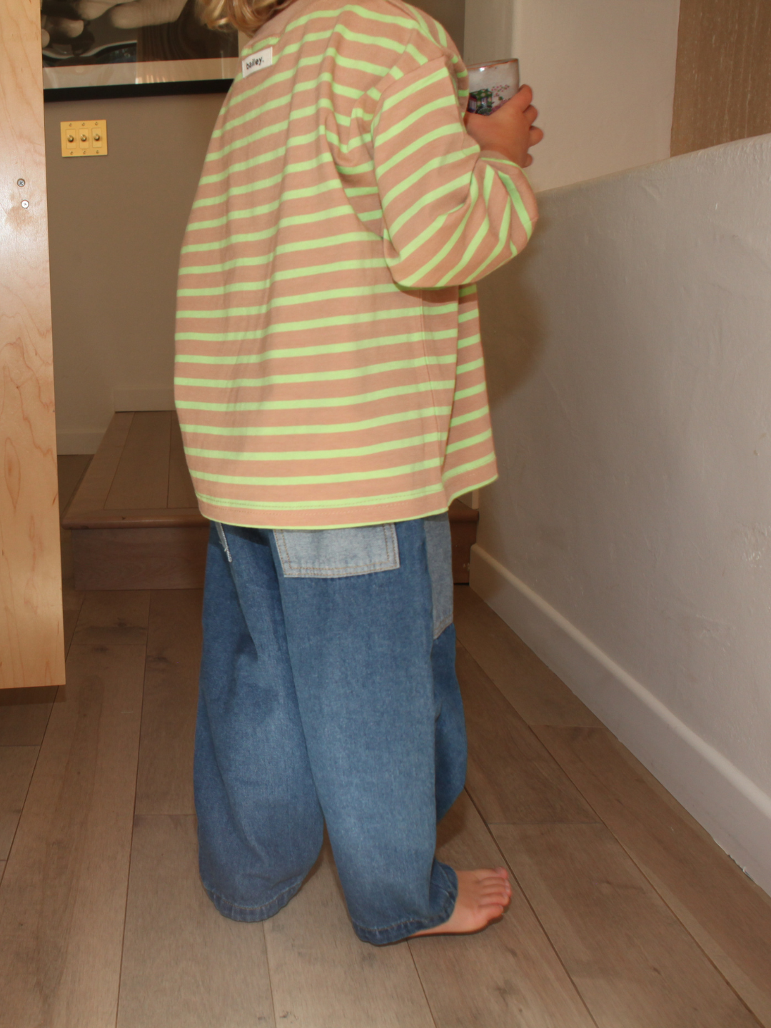 Dark Wash | A child wearing a striped shirt and denim pants standing on a wooden floor.