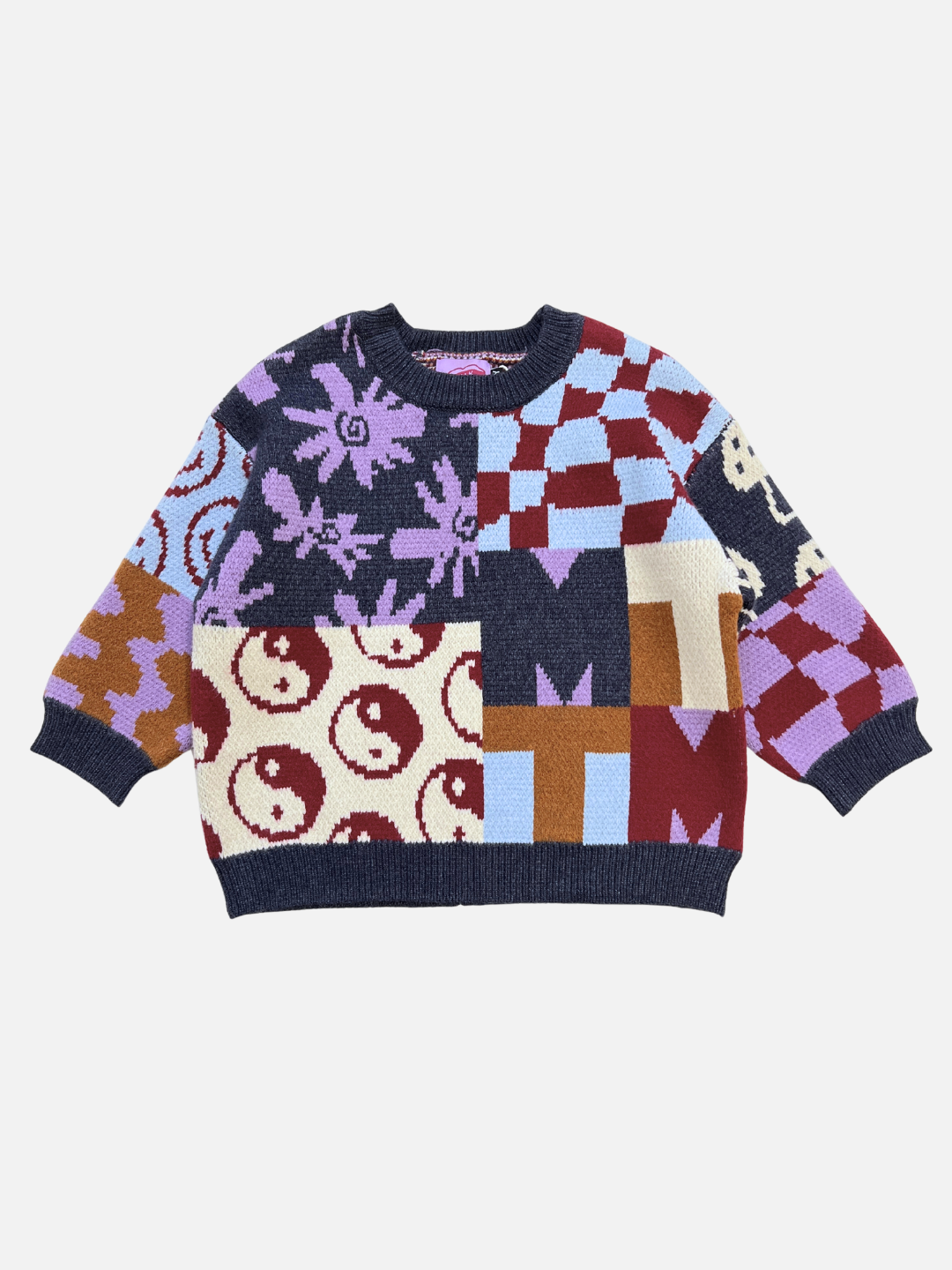 The EVERYTHING SWEATER is a soft knit featuring a patchwork design with yin-yang symbols, flowers, wavy checkers, and geometric shapes in purple, red, cream, blue, and brown tones.