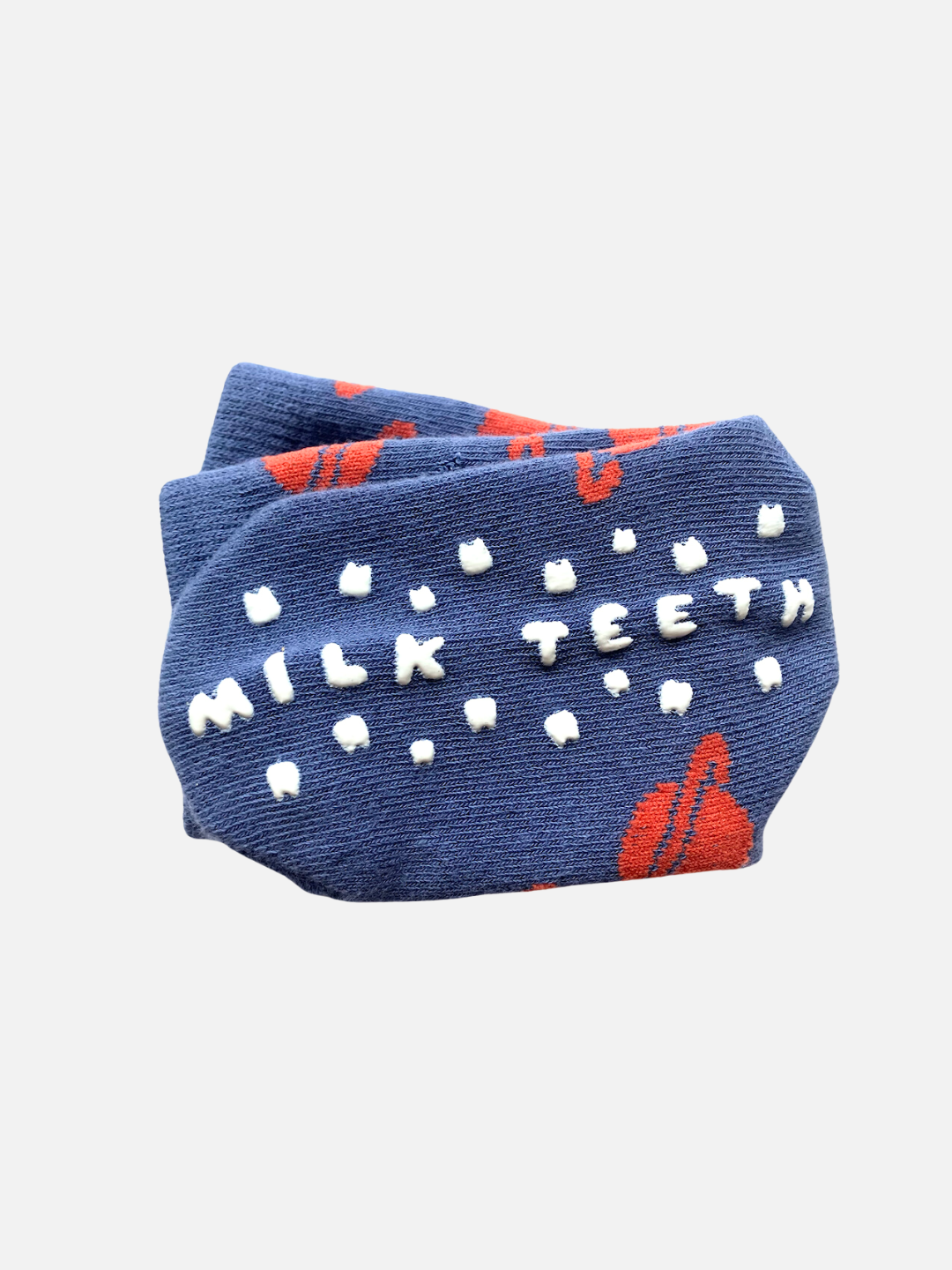 Slate Spacecamp | This blue fabric folded around the foot features white raised text spelling "MILK TEETH" and small teeth-like shapes, accented with red abstract designs. Made from stretchy material that feels as soft as a plush toy, these GRIP SOCKS ensure comfort while offering charming aesthetics.