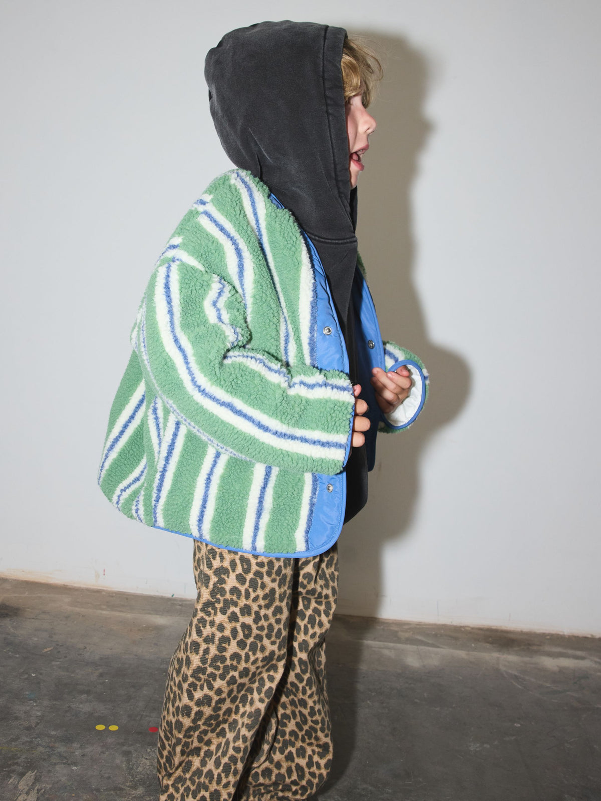 Side view of a child in the green striped sherpa jacket, with the hoodie's hood up.