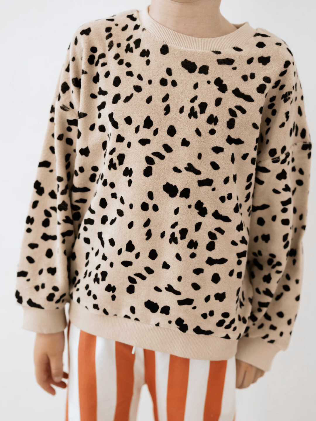 A person wearing the DALMATIAN TERRY SWEATSHIRT and red-and-white striped pants, part of our new arrivals, stands against a plain background.