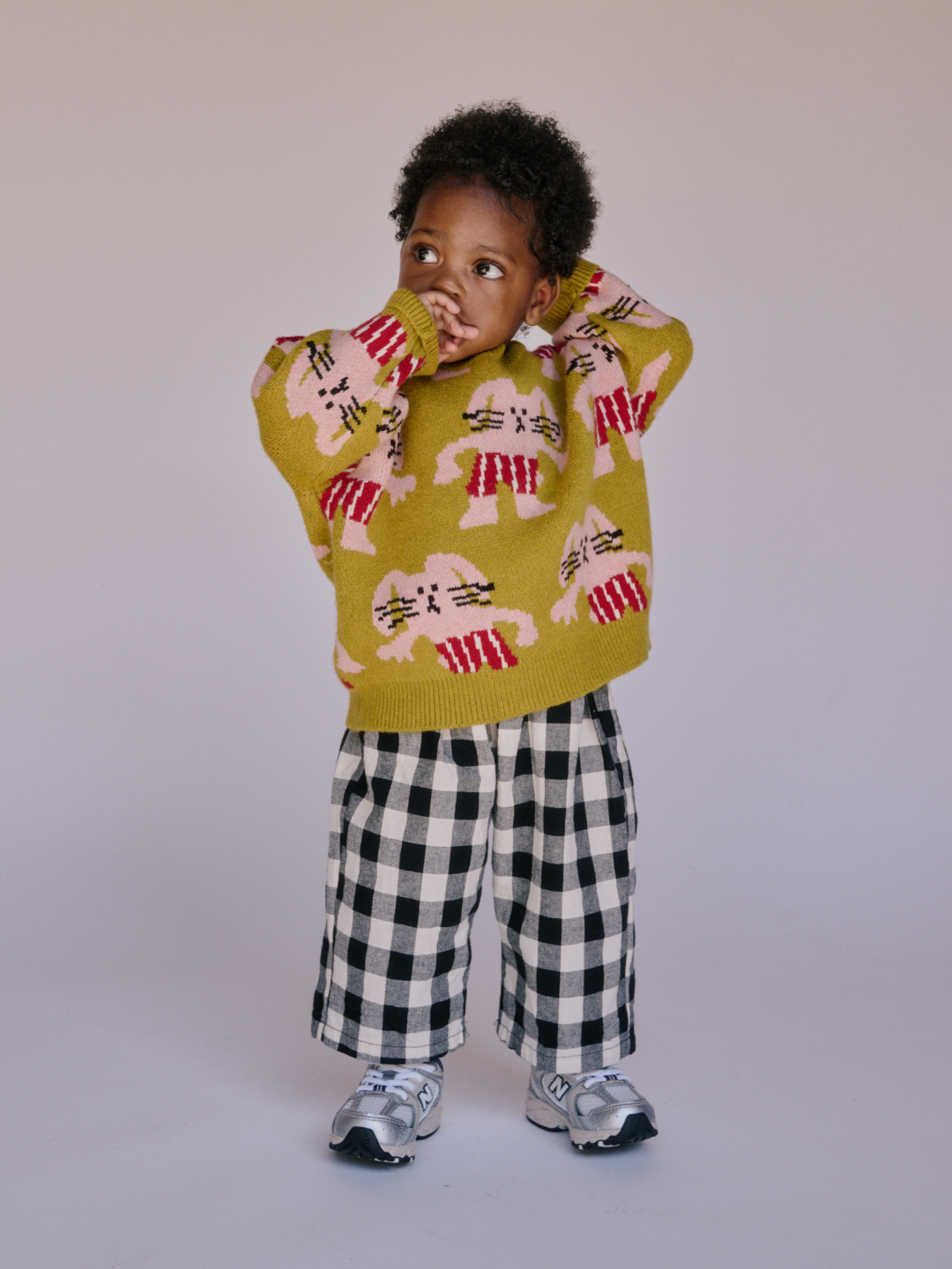 Chartreuse | A young child stands against a plain background, dressed in the MAX SWEATER featuring bunny designs, plaid pants, and gray sneakers.
