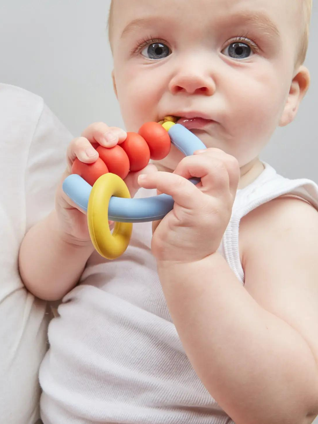 Primary | Baby chewing blue semicircle teether strung with red beads and yellow ring
