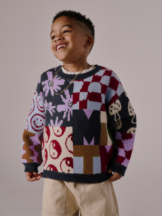 Second image of The EVERYTHING SWEATER is a soft knit featuring a patchwork design with yin-yang symbols, flowers, wavy checkers, and geometric shapes in purple, red, cream, blue, and brown tones.