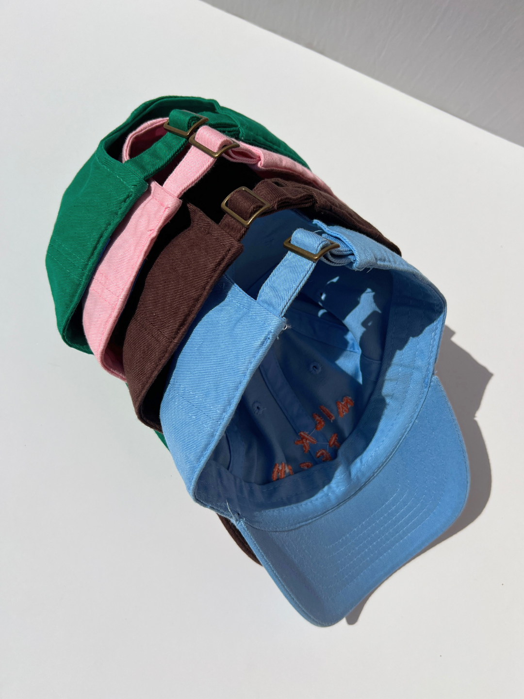 Pink | A stack of Milk Teeth embroidery caps showcasing the adjustable backings