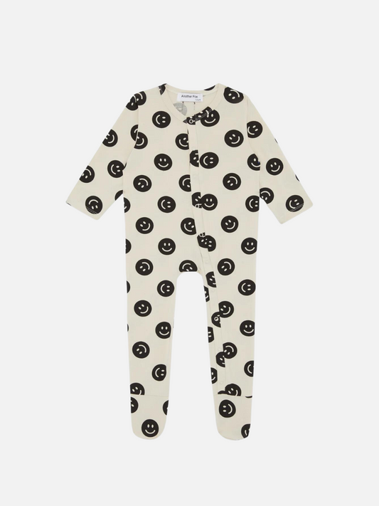Image of A front view of the cream colored, long sleeve, and full pant sleepsuit with a black smiley face pattern.
