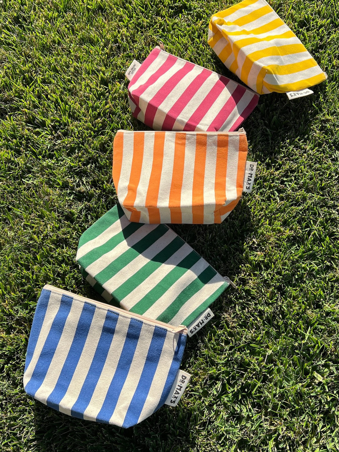 Five ORGANIC COTTON ZIPPER BAGs in yellow, green, red, and blue are laid on grass—ideal for organizing diaper bags and made from durable organic cotton.