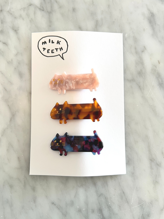Second image of Three kids' barrettes in the shape of elongated cats: one pink, one ginger, one purple