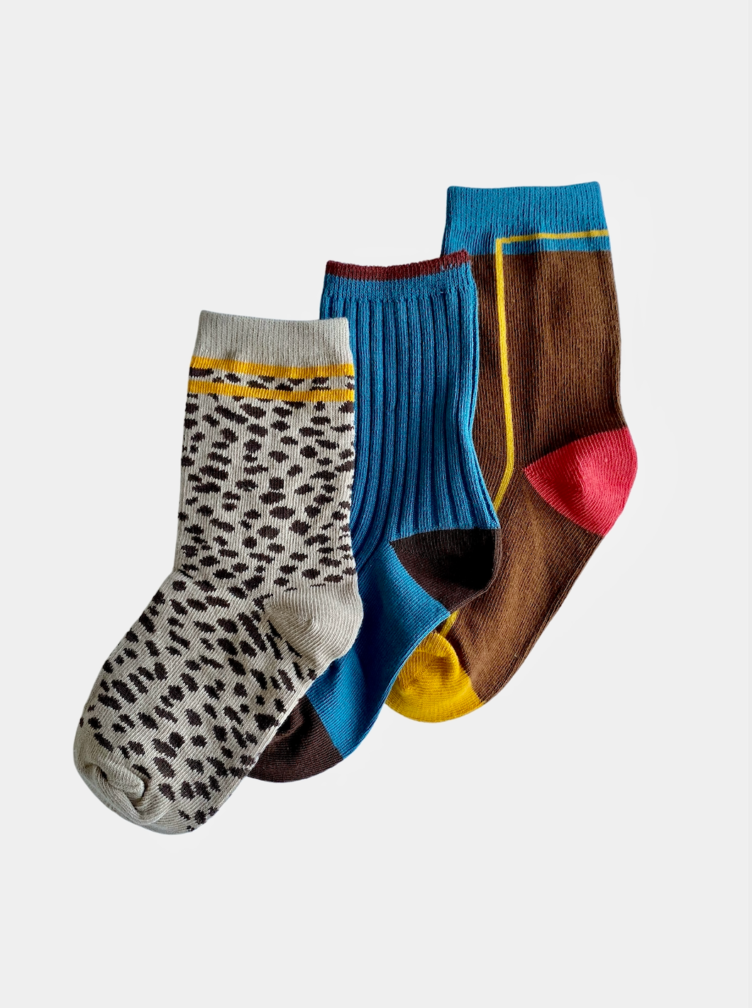 A trio of kids' ankle socks. One pair with brown spots and yellow stripes at the top, one in sky blue with brown toes, heels and tops, one in brown with yellow, read and blue details