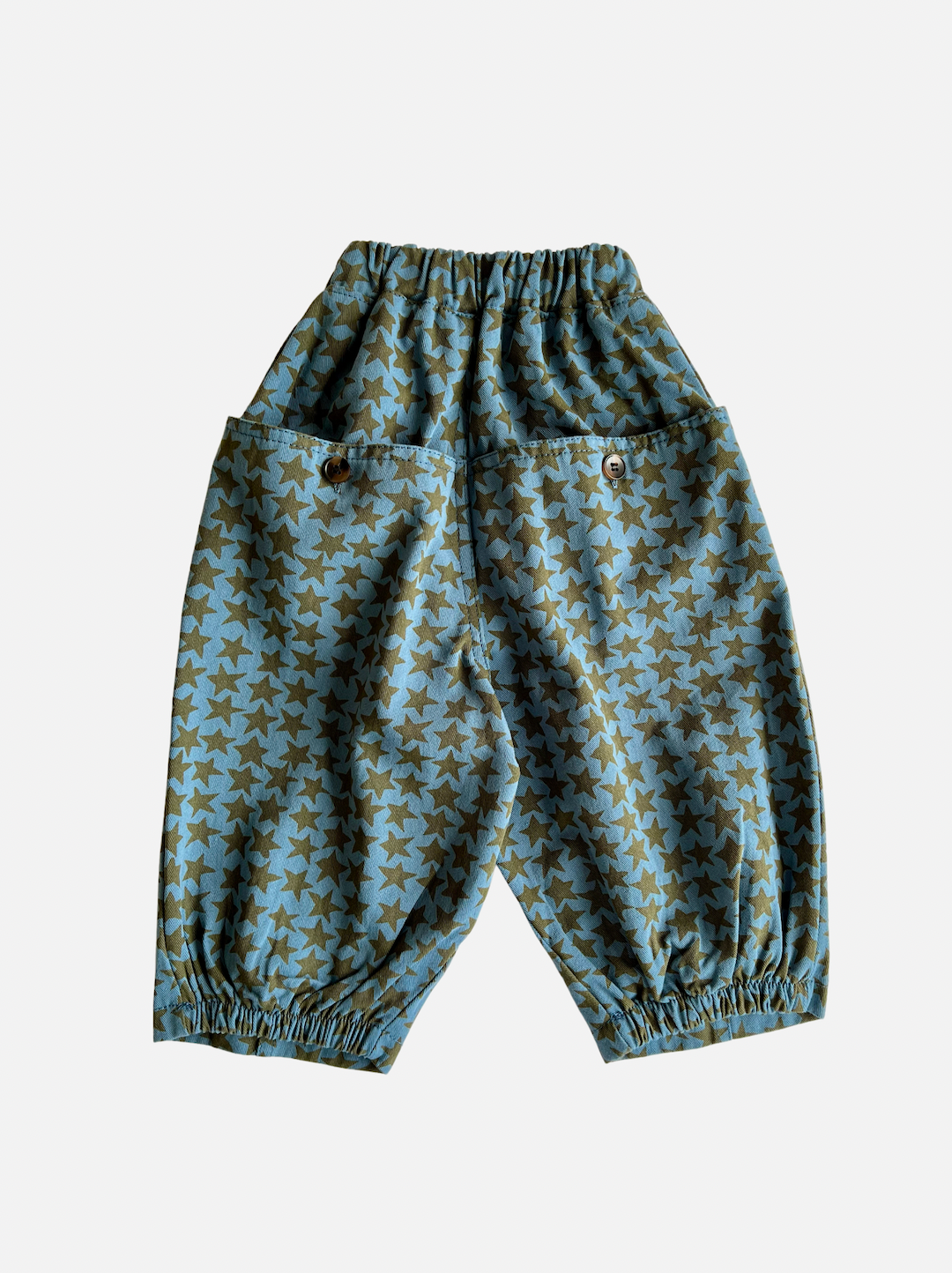 Slate | A pair of kids' pants in slate blue with an olive green star pattern, and buttoned back pockets, rear view