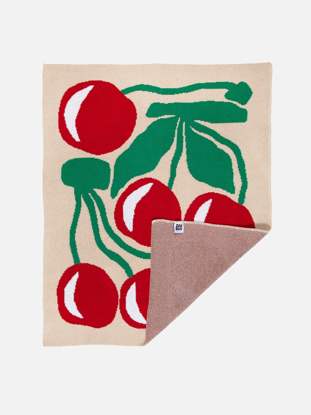 A mini blanket patterned with red cherries and green leaves on a taupe background, showing part of the plain reverse side
