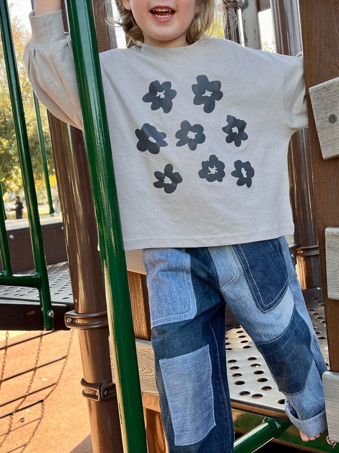 A child on a jungle gym wearing a kids' tee shirt in soft gray with dark gray flowers, sleeves gathered at the cuff, over two-tone denim pants