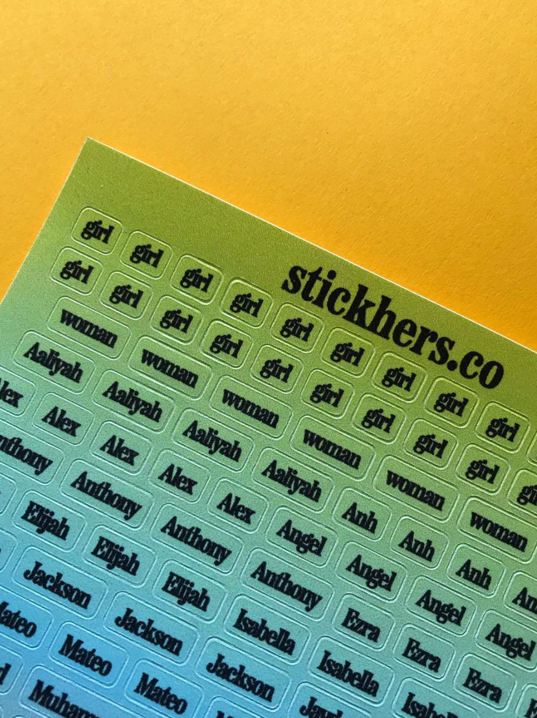 A sheet of StickHERS gender equity stickers on a yellow background, featuring various names and words, including "girl," "woman," "Aaliyah," "Alex," "Angel," "Anthony," "Jackson," "Isabella," and "Mateo.