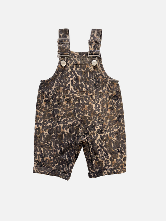 Image of The BLYTHE LEOPARD DUNGAREE BABY is a pair of unisex, organic cotton leopard-print overalls for toddlers, featuring adjustable straps with metal buckles and buttons—an essential wardrobe staple.
