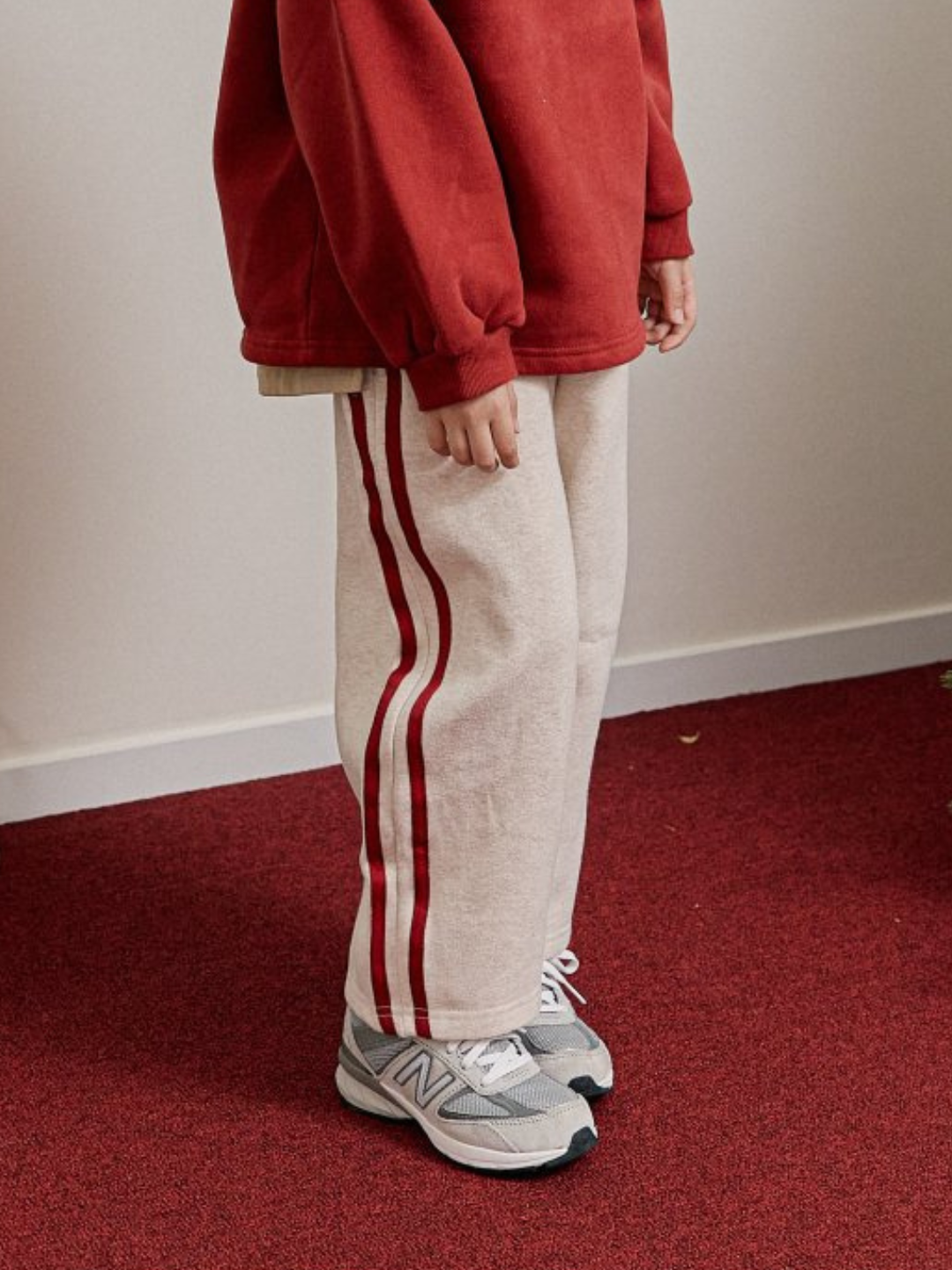 A child is wearing Varsity Pant in Oatmeal with sneakers and red pullover