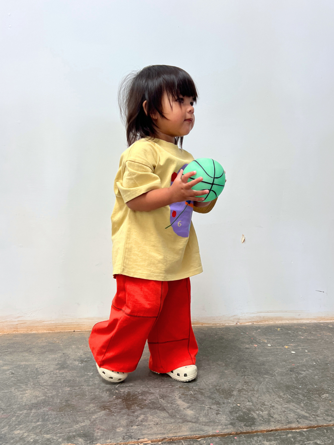 Red | Child holding a green ball against a plain background