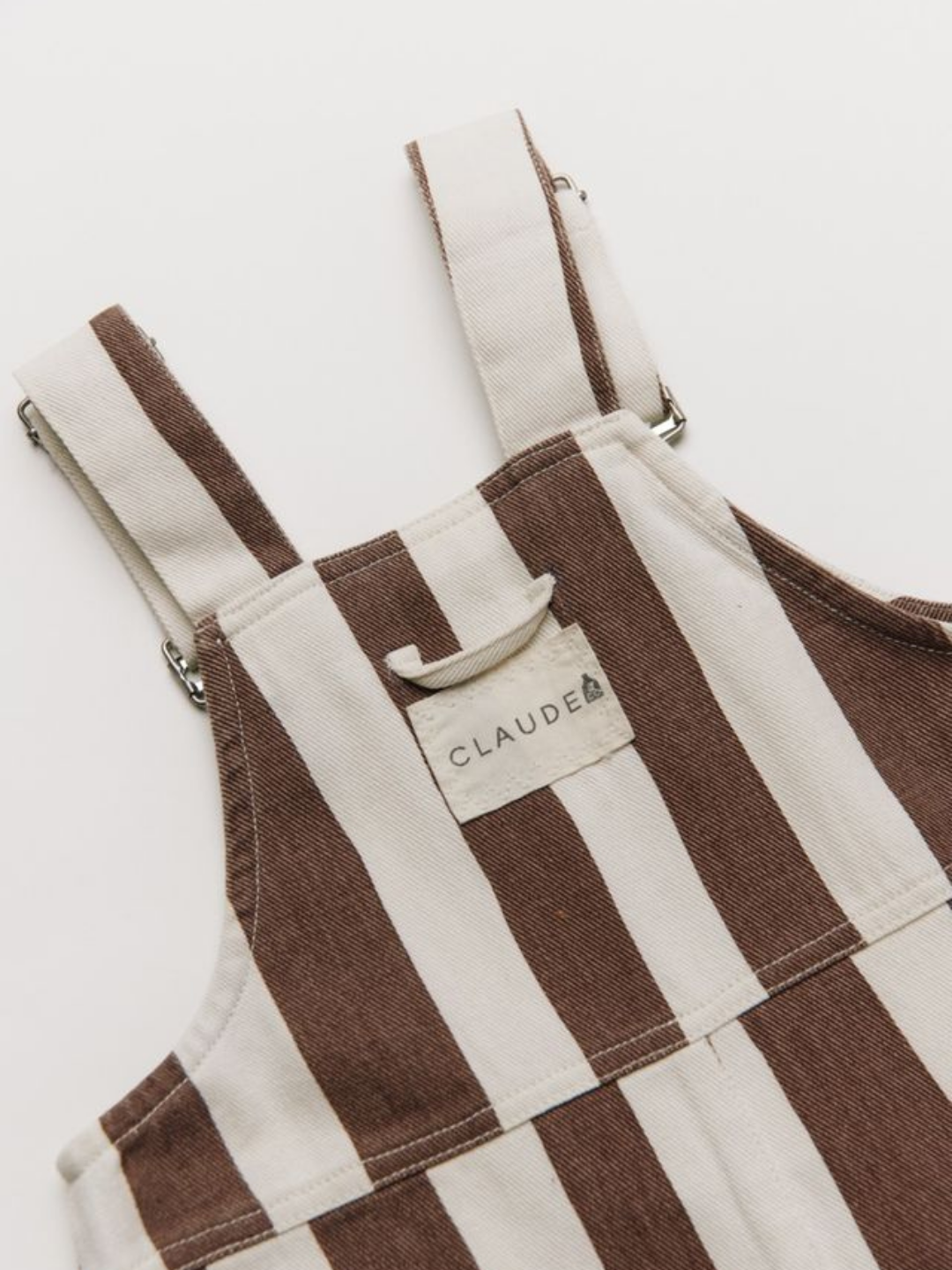 The BLYTHE CHOC STRIPE DUNGAREE features brown and white vertical stripes, adjustable straps, and a front label that reads "CLAUDE.