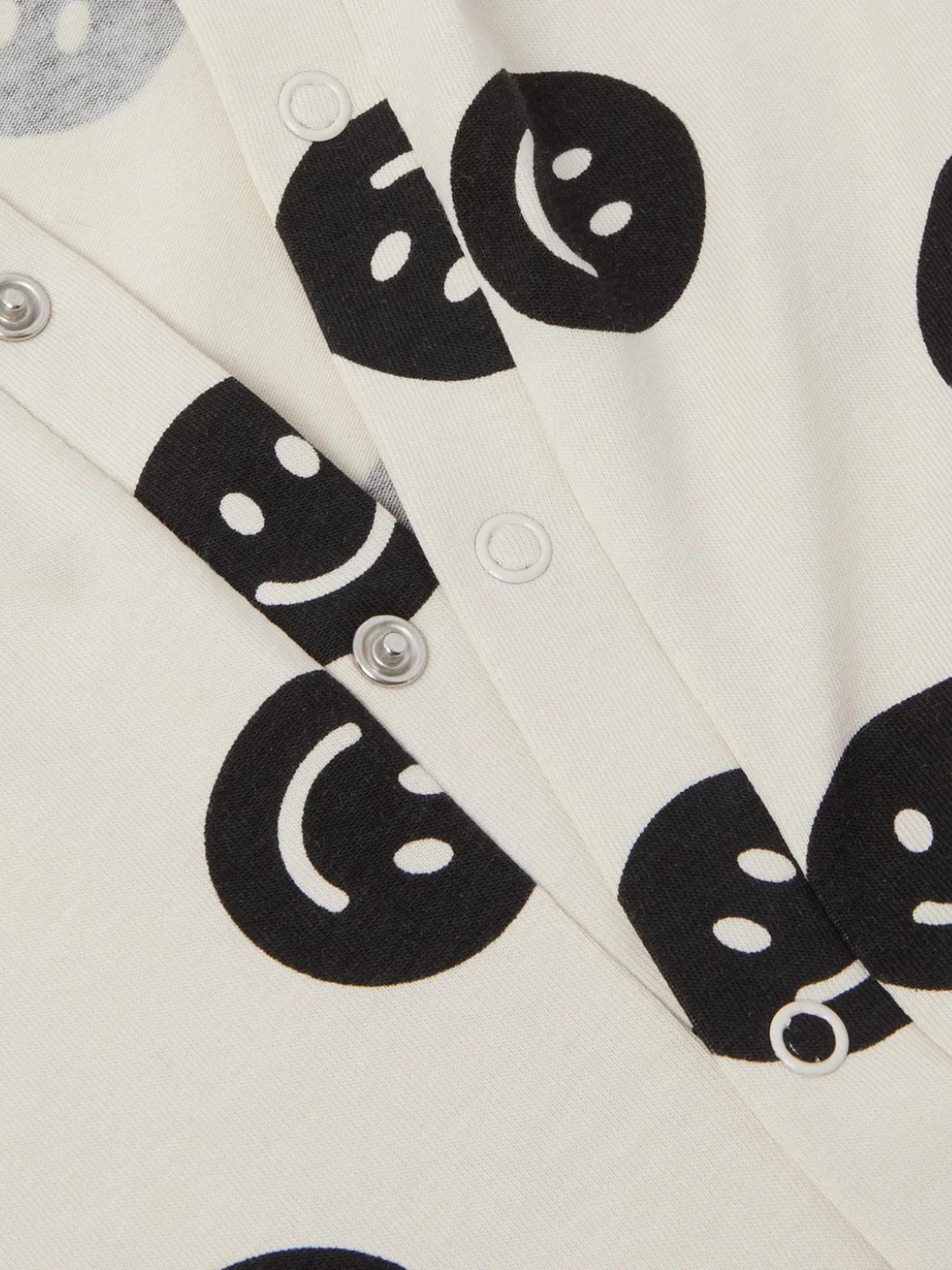 A zoomed in front view of the cream colored, long sleeve, and full pant sleepsuit with a black smiley face pattern.