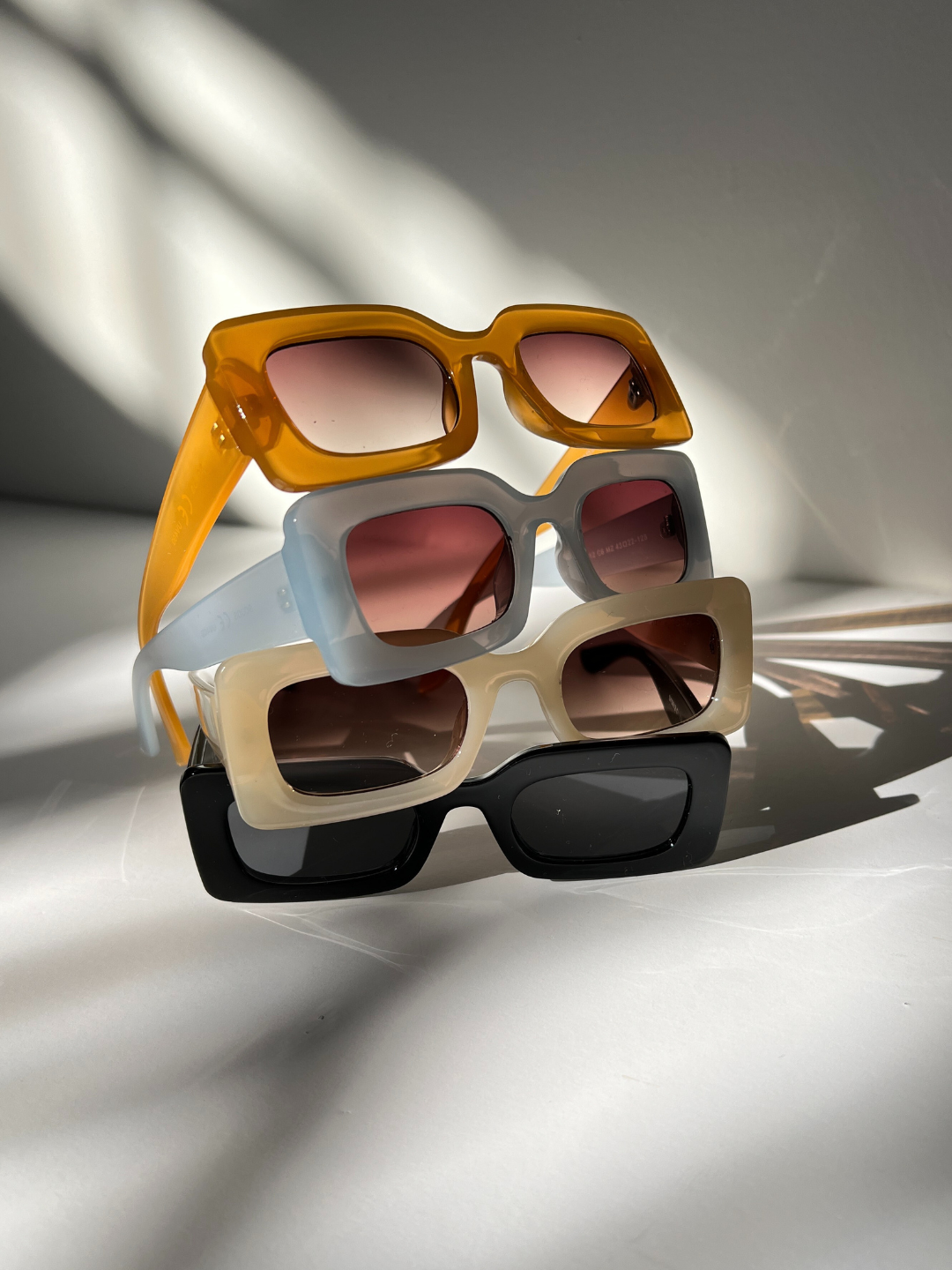 Group of kids rectangle sunglasses, stacked on top of each other, in orange, blue, orange, cream, and black, on a white background.