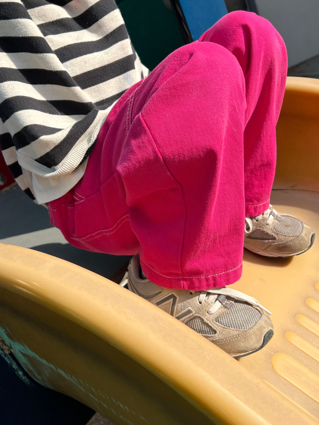 Magenta | A child wearing a striped shirt and Topstitch Twill Pants in pink sits on the slide with sneakers. The soft cotton twill fabric and elastic waistband offer ultimate comfort for playtime adventures.