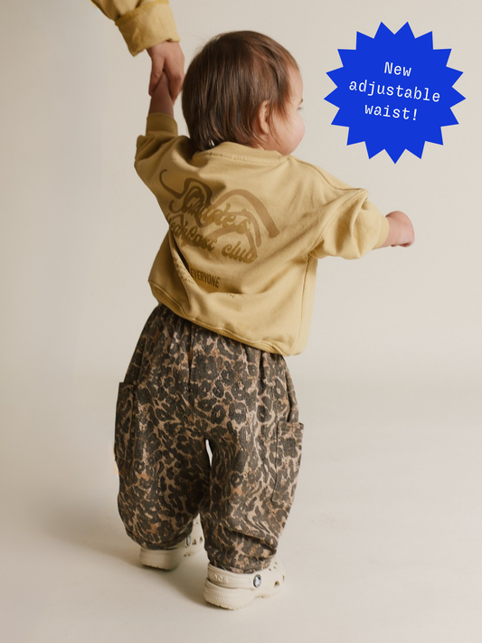 Second image of The EMERSON LEOPARD TROUSER is a unisex piece for toddlers, made with soft organic cotton. It has a leopard print design on a crisp white background, featuring an elastic waistband and large pockets.