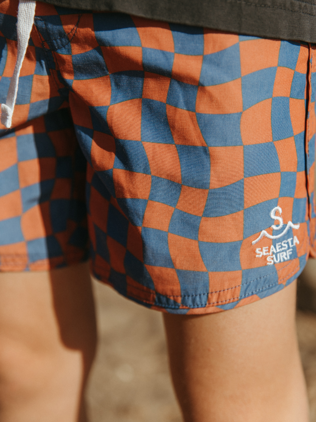 A close up on the kid's Wavy Checks Boardshort highlighting the print and Siesta Surf logo. 