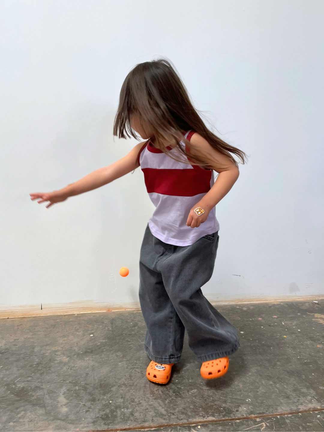 Purple/Maroon | A child in a TRACK TANK, relaxed wide pants, and orange clogs is swatting at an orange ball indoors.