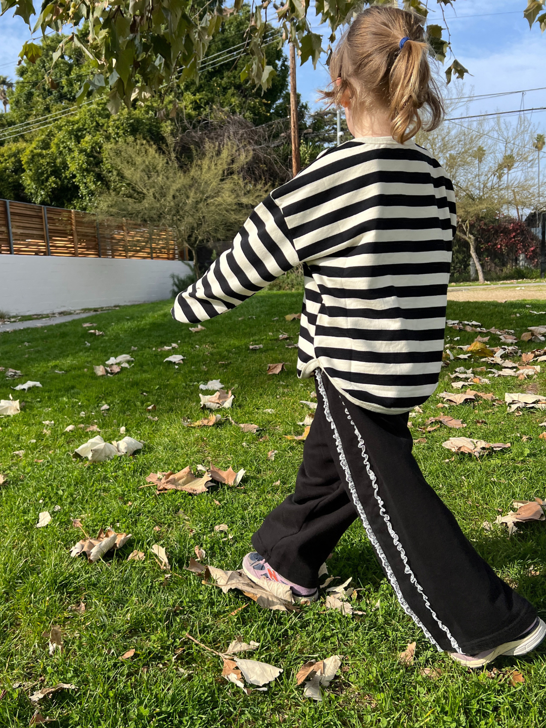 A child is wearing Relay pants with striped long sleeve tee and purple sneakers