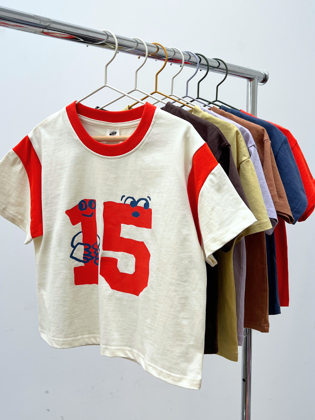 Children's t-shirt with red number 15 design on a rack with other shirts.