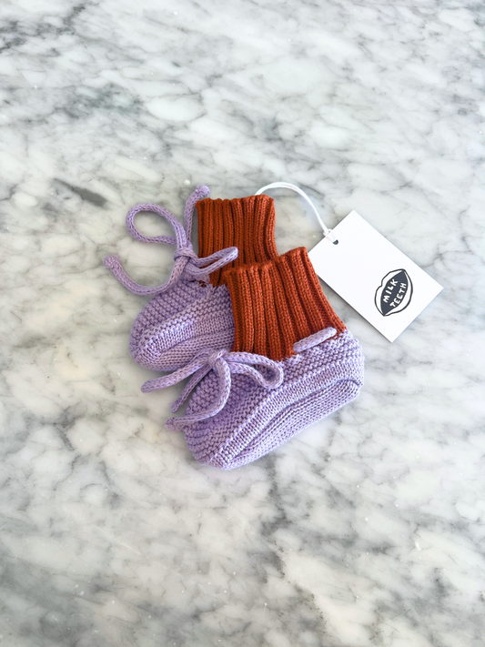 Second image of Purple | Knitted baby bootie in lavender purple with a red ribbed cuff and a purple tie closure