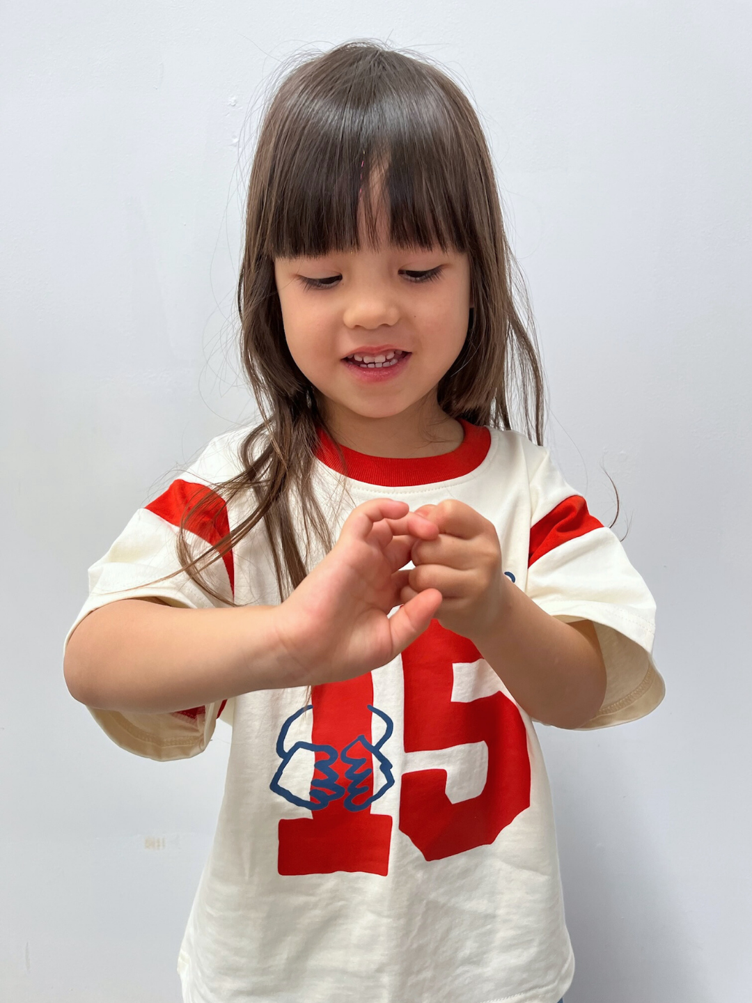 Child wearing a white and red sports jersey with number 15 on a plain background
