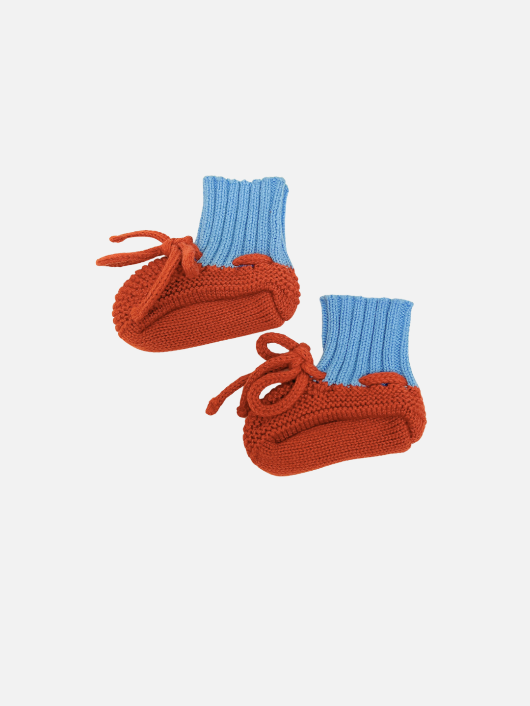 A pair of cotton knit baby booties with textured rust-orange knit soles and light blue knit cuffs, featuring bow tie closures, set against a plain light gray background.