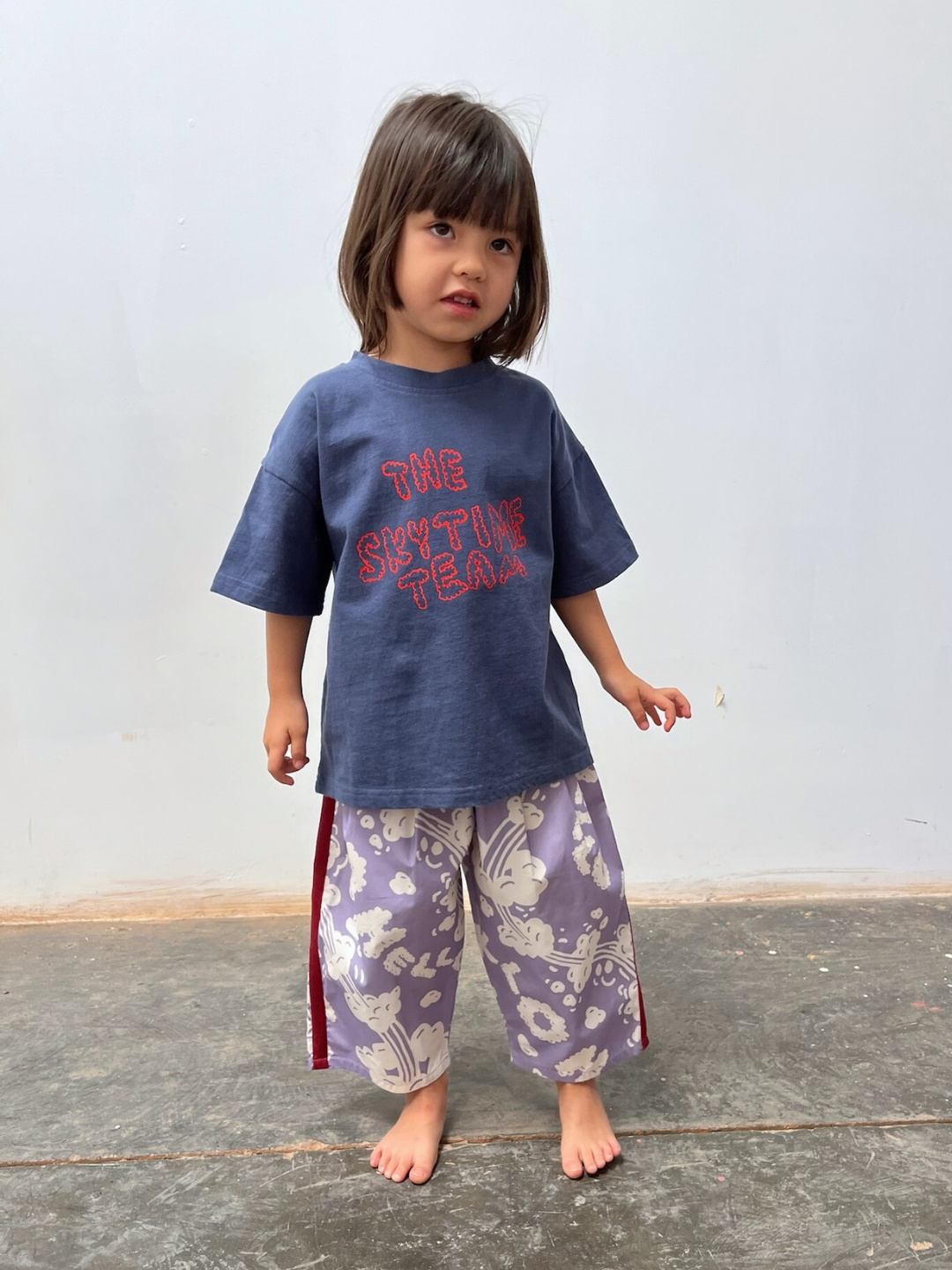 Blue | Child wearing a blue shirt with text and patterned pants on a plain background