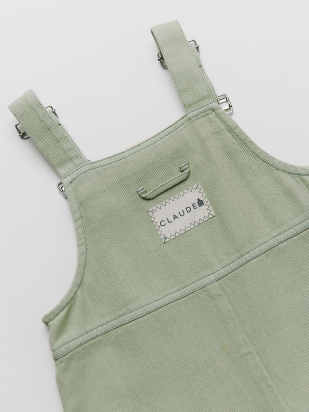 The BLYTHE MINT DUNGAREE features light green overalls with adjustable straps and a stitched rectangular "CLAUDE" label on the chest, shown on a white background.