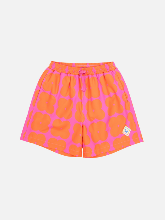 Image of Front of Clover Shorts. Bright orange clover shapes on a bright pink background. Has an elastic waist with a tie and small logo on bottom right corner.