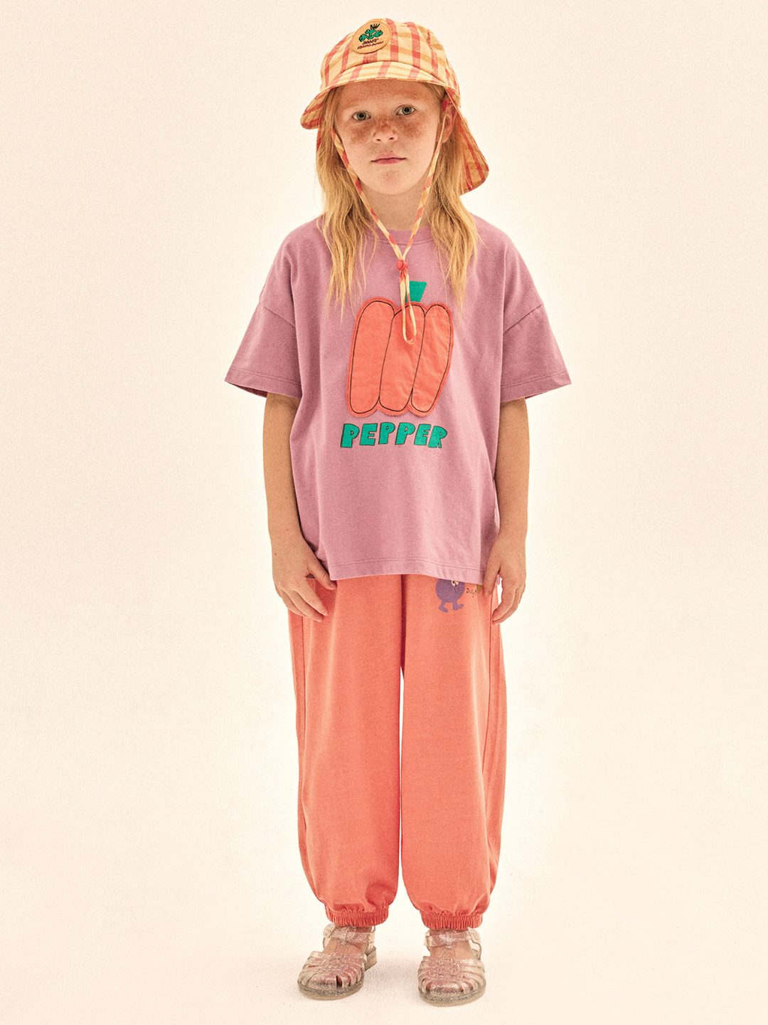 Child wearing a pink t-shirt with a graphic design and peach-colored pants on a beige background