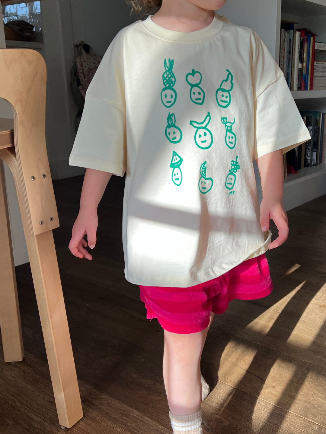 Cream | A child is wearing a cream Fruit Face tee with pink shorts indoors.