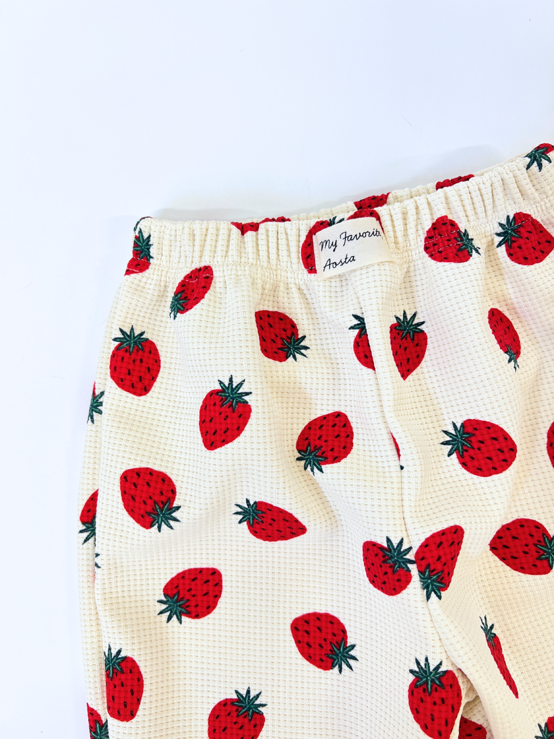 These adorable cream-colored STRAWBERRY WAFFLE JOGGERS feature a strawberry print, waffle-textured fabric, and a white "My Favorite" and "Aoia" label near the waistband, from a trendy Korean kids brand.