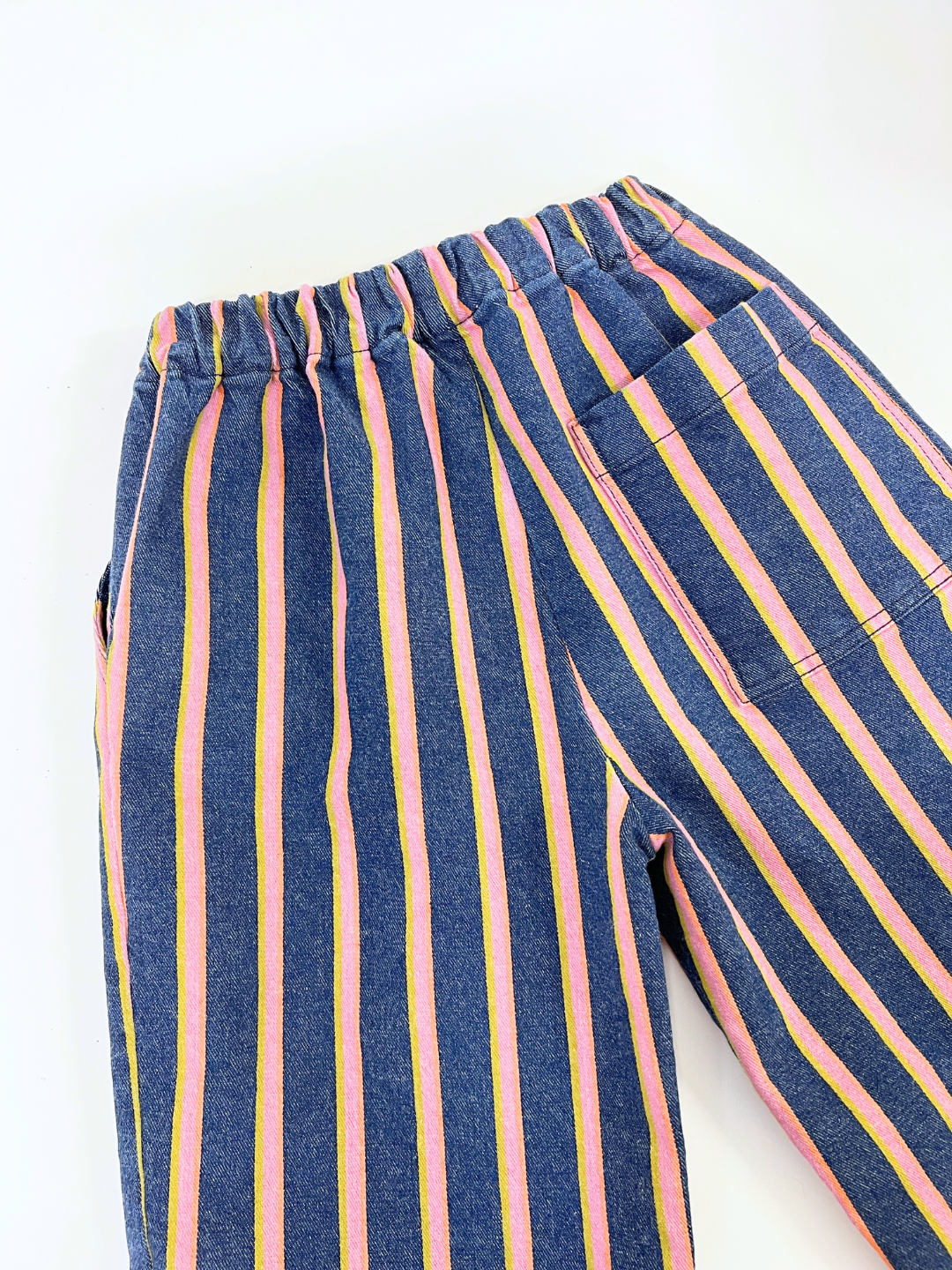 The EVER DENIM WIDE LEG STRIPED TROUSERS feature vibrant pink, yellow, and blue vertical stripes in a unisex design. An elastic waistband and visible pocket add functionality while adding fun to any minimalist style.